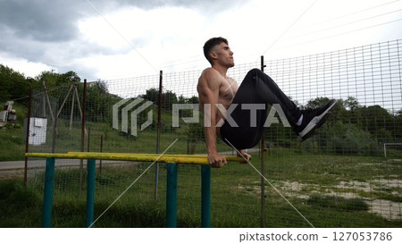 Strong guy training abdominal muscles on parallel bars at sports ground. Young shirtless sportsman exercising at nature. Sporty athlete working out at nature. Concept of active sportive lifestyle 127053786