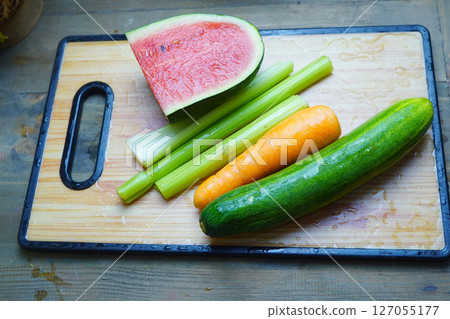 Various cut vegetables and watermelon pieces are arranged on a wooden cutting board 127055177