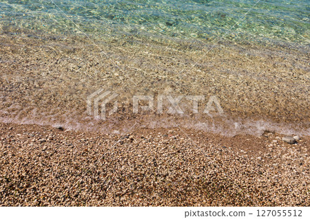 Clear water on pebble shore. Coastal texture, summer serenity, and natural detail of Mediterranean beach environment. Clear water on pebble shore. Coastal texture, summer serenity, and natural detail of Mediterranean beach environment. 127055512