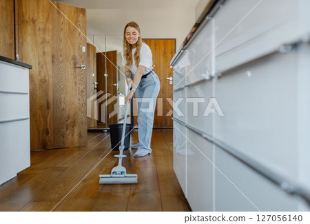 A Young Woman Carefully Cleaning the Hardwood Floor in a Stylish Modern Kitchen Environment 127056140