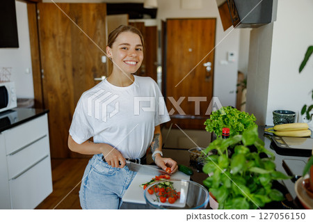 A Cheerful Young Woman Happily Cooking in Her Modern Kitchen with Fresh Ingredients and Joy A Cheerful Young Woman Happily Cooking in Her Modern Kitchen with Fresh Ingredients and Joy 127056150