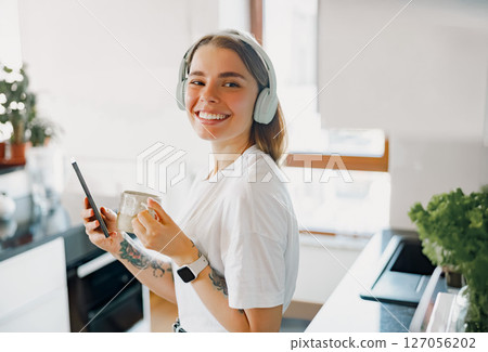 A Cheerful and Joyful Young Woman Experiencing Enjoyable Music in a Modern Kitchen Setting A Cheerful and Joyful Young Woman Experiencing Enjoyable Music in a Modern Kitchen Setting 127056202