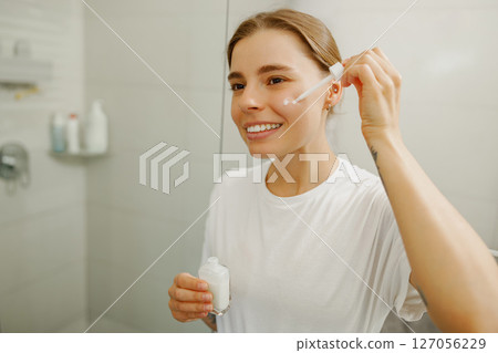 Skincare Routine A Young Woman Applying Serum in Her Bright and Clean Bathroom Area 127056229