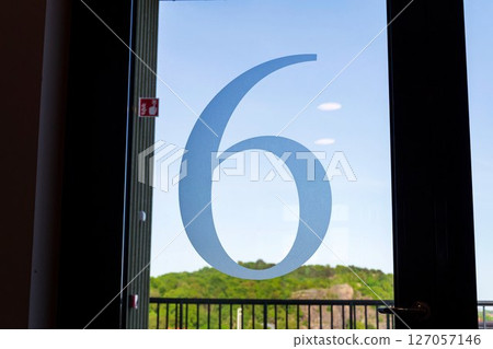 Number 6 on the glass door of an apartment building, sunny day 127057146