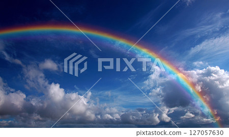 Vibrant rainbow arches across a blue sky filled with fluffy clouds, showcasing nature's beauty after a rain shower 127057630
