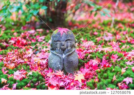 Jizo smiling Buddha by red autumn maple leaf at Enkoji garden, Kyoto 127058076