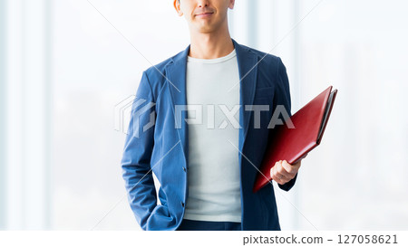 Smiling male businessman holding a binder Smiling male businessman holding a binder 127058621