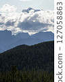 Majestic mountains rising above evergreen forest under cloudy sky 127058863