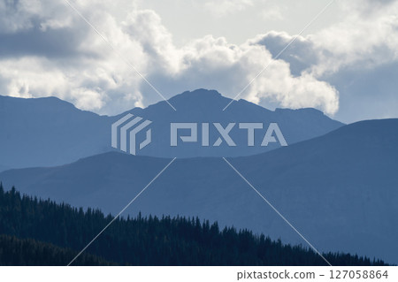 Majestic mountain peaks loom over a serene forest landscape Majestic mountain peaks loom over a serene forest landscape 127058864