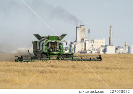 Farmer harvesting wheat crop with combine harvester near factory Farmer harvesting wheat crop with combine harvester near factory 127058922