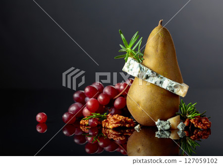 Blue cheese with pear, walnuts, red grapes, and rosemary on a black background. 127059102