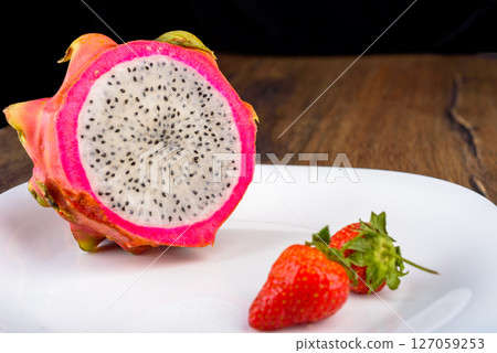 Half a pitahaya or dragon fruit on a plate with strawberries. Half a pitahaya or dragon fruit on a plate with strawberries. 127059253