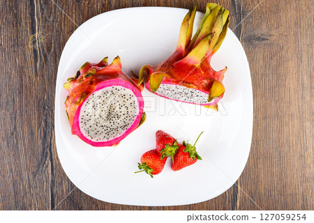 Top view of two halves of Dragon fruit or Pitaya and three strawberries on a white plate. Top view of two halves of Dragon fruit or Pitaya and three strawberries on a white plate. 127059254