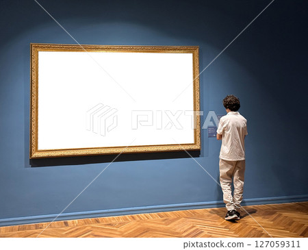 Blank art frame hanging on a white wall in a gallery or museum space. Visitor walk through the 127059311