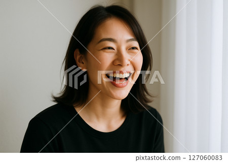 A woman laughing by a window with natural light streaming in 127060083