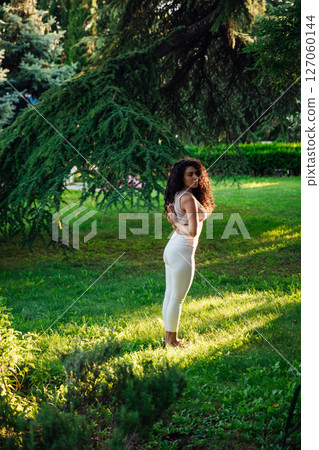 brunette woman doing gymnastics yoga asana on the grass in the park 127060144