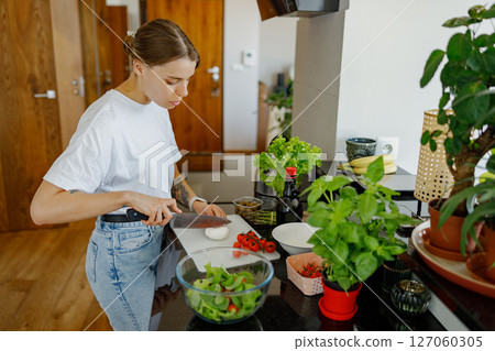 A woman is diligently cooking a fresh salad in a modern kitchen, surrounded by vibrant herbs 127060305