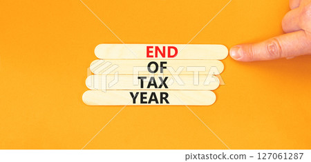 End of tax year symbol. Concept words phrase End of tax year on beautiful wooden stick. Businessman's hand. Beautiful orange paper background. Business End of tax year concept. Copy space. End of tax year symbol. Concept words phrase End of tax year on beautiful wooden stick. Businessman's hand. Beautiful orange paper background. Business End of tax year concept. Copy space. 127061287
