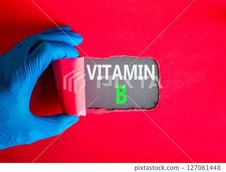 Vitamin B symbol. Concept words Vitamin B on beautiful grey paper. Doctor hand in blue medical glove. Beautiful red background. Medical healthy lifestyle Vitamin B concept. 127061448