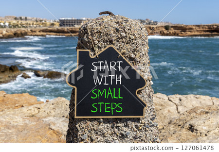 Start with small steps symbol. Concept words phrase Start with small steps on beautiful black blackboard. Beautiful stone blue sea sky background. Business Start with small steps concept. Copy space. 127061478