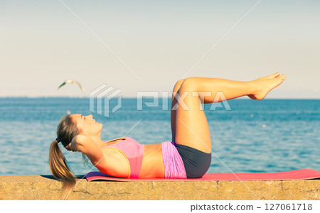 Woman doing sports exercises outdoors by seaside 127061718