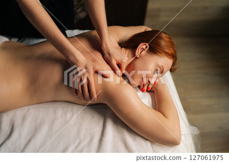 High-angle view of female client getting relaxing back massage from professional massage therapist lying resting on table, experiencing therapeutic wellness at luxurious spa setting, close-up top view High-angle view of female client getting relaxing back massage from professional massage therapist lying resting on table, experiencing therapeutic wellness at luxurious spa setting, close-up top view 127061975