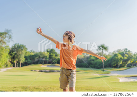 Boy wearing a pilot hat running through the grass with a toy airplane, dreaming of adventures. Childhood, imagination, and freedom concept 127062564