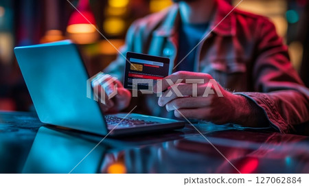 Person Holding Credit Card While Using Laptop in Low-Light Setting 127062884