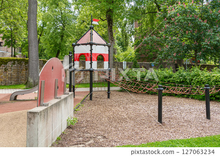 Colorful playground with a castle-themed structure, featuring a slide and rope bridge in a lush park setting. Ideal for childrens outdoor activities and imaginative play. Colorful playground with a castle-themed structure, featuring a slide and rope bridge in a lush park setting. Ideal for childrens outdoor activities and imaginative play. 127063234