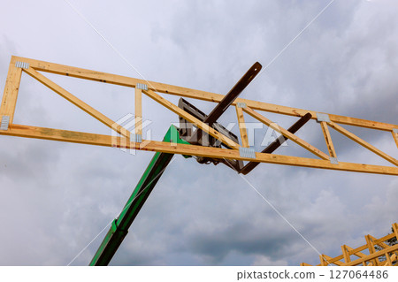 Workers operate a lift to install wooden trusses on a building structure as dark clouds loom overhead. 127064486