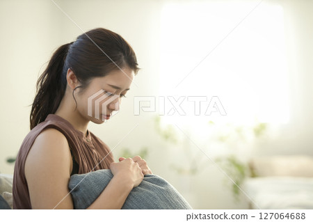 一名 20 多歲的女性身體不適,坐在沙發上 一名 20 多歲的女性身體不適,坐在沙發上 127064688