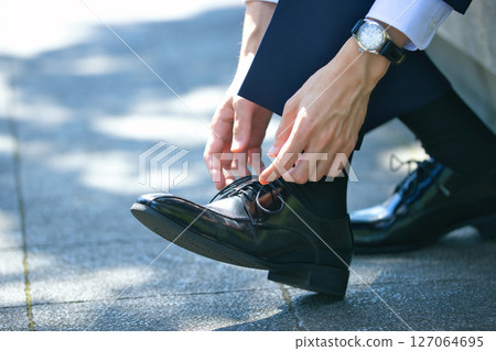 一位穿著西裝的年輕男子正在繫上商務鞋的鞋帶 一位穿著西裝的年輕男子正在繫上商務鞋的鞋帶 127064695