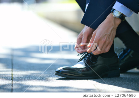The feet of a young man in a suit tying the laces of his business shoes 127064696
