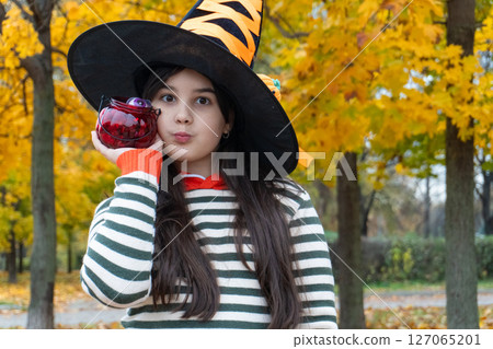 Young girl in witch hat holding candy jar during halloween in autumn park Young girl in witch hat holding candy jar during halloween in autumn park 127065201