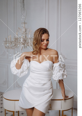 Young woman in white dress posing near table in classic white room with tiled floor and lemons Young woman in white dress posing near table in classic white room with tiled floor and lemons 127065266