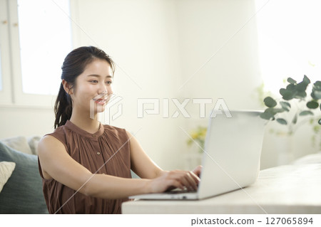 一位二十多歲的女士在客廳裡用筆記型電腦工作 127065894