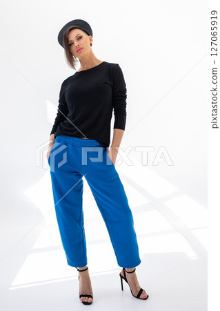 Elegant woman in black windbreaker jacket, blue pants and nautical hat on white background. Fashionable female in ocean French style. Studio photography. Vertical photo. High quality photo 127065919