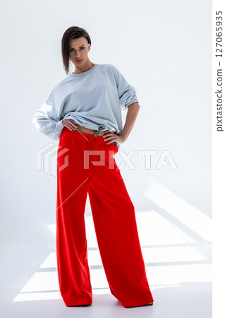 Young woman in gray sweatshirt and red pants on white background. Studio photography. Vertical photo. High quality photo 127065935