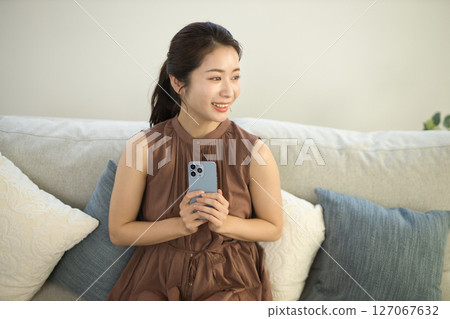 A woman in her twenties sitting on a sofa and operating a smartphone A woman in her twenties sitting on a sofa and operating a smartphone 127067632