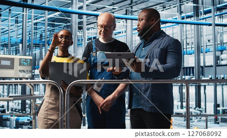 Engineers talking with manager overseeing smart factory, showing collected metrics. Technicians receiving feedback from supervisor in industry 4.0 industrial plant equipped with sensors, camera A 127068092