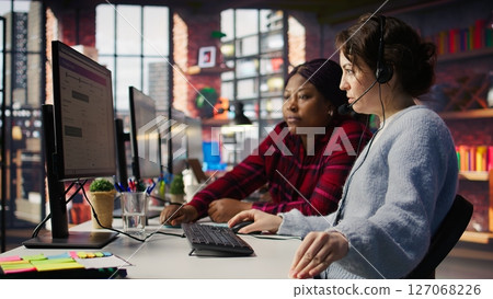 Call center team leader going over paperwork files next to colleague at PC desk. Customer support manager explaining company documentation to intern accommodating with job, camera B Call center team leader going over paperwork files next to colleague at PC desk. Customer support manager explaining company documentation to intern accommodating with job, camera B 127068226