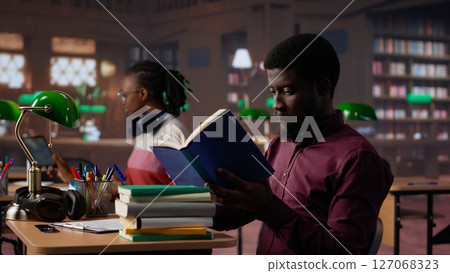 Young girl reading a literature book to collect citations for her bachelor paper, ensuring a plagiarism free diploma paperwork at the university library. Student takes notes on textbook. Camera A. Young girl reading a literature book to collect citations for her bachelor paper, ensuring a plagiarism free diploma paperwork at the university library. Student takes notes on textbook. Camera A. 127068323