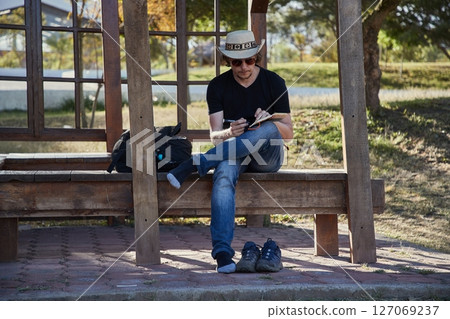 Man writing journal notes sitting on bench 127069237