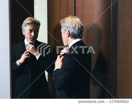 Middle-aged man looking in the mirror and grooming himself 127069802