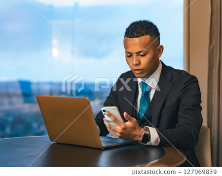 A businessman working with a laptop and smartphone in a high-rise office 127069839