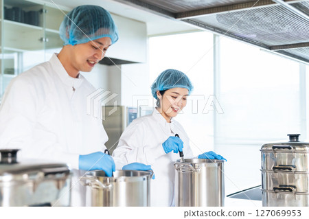 一位身穿衛生白大褂的女廚師在廚房、學校午餐中心、自助餐廳的大鍋裡做飯 一位身穿衛生白大褂的女廚師在廚房、學校午餐中心、自助餐廳的大鍋裡做飯 127069953