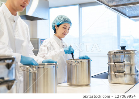 A group of chefs wearing sanitary white coats cooking in a large pot in the kitchen, school lunch center, cafeteria 127069954
