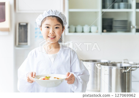 A girl on school lunch duty wearing a white coat and holding a plate A girl on school lunch duty wearing a white coat and holding a plate 127069962