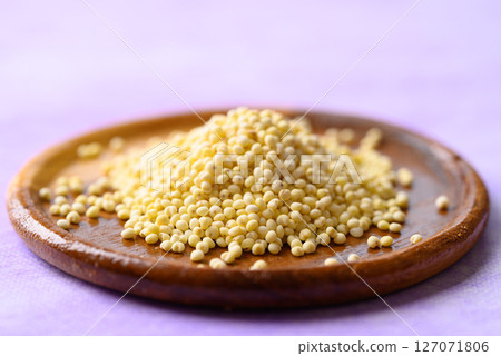 Yellow millet grain on wooden plate with purple background, Food ingredient 127071806
