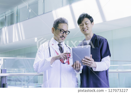 A portrait of two doctors talking while looking at a tablet in a hospital. Photo courtesy of Sky Perfect TV Tokyo Media Center. A portrait of two doctors talking while looking at a tablet in a hospital. Photo courtesy of Sky Perfect TV Tokyo Media Center. 127073227